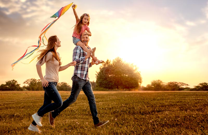 young girl sitting on her fathers shoulders while flying a kite